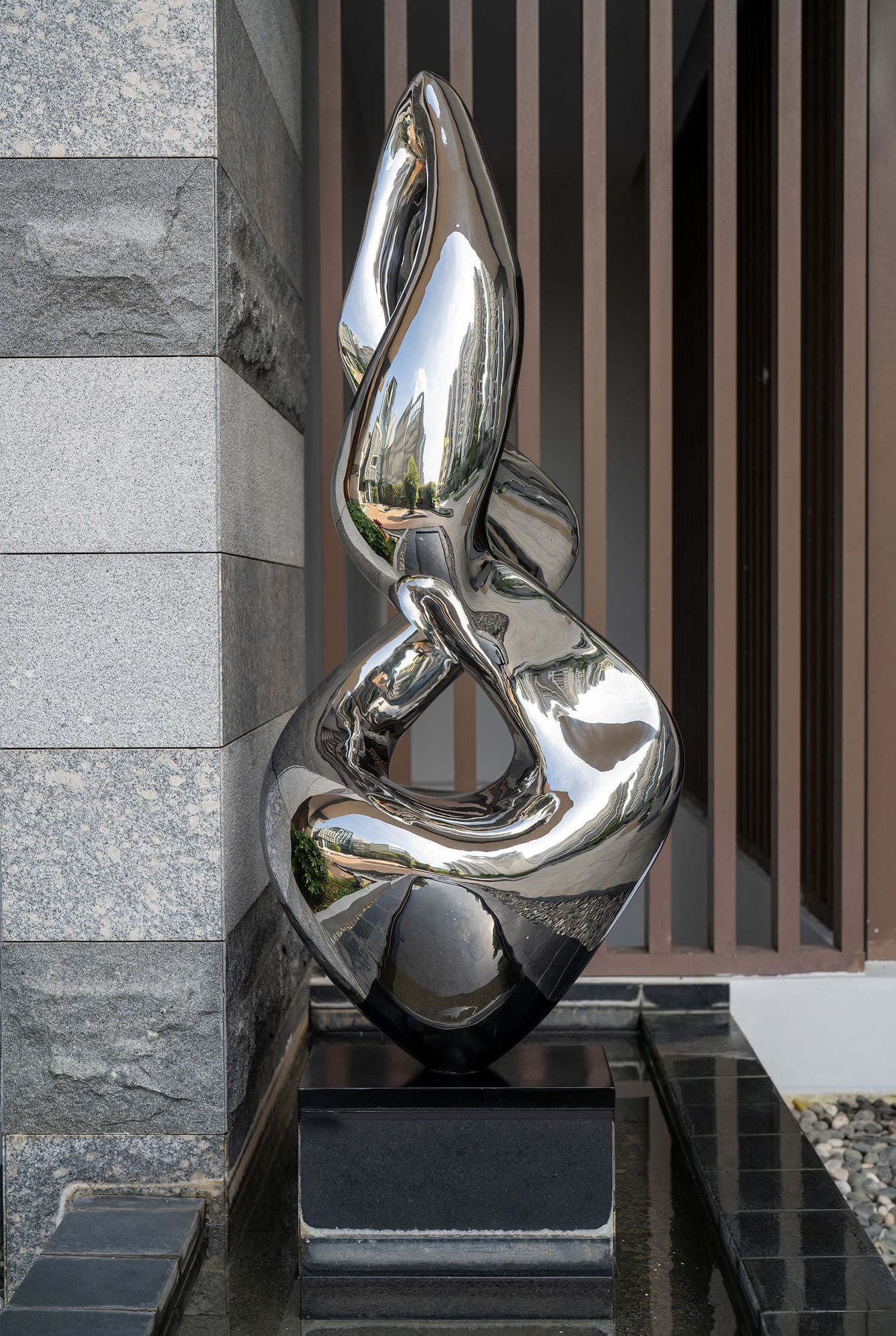 The polished stainless steel sculpture seen head on, reflecting the towers and greenery around it